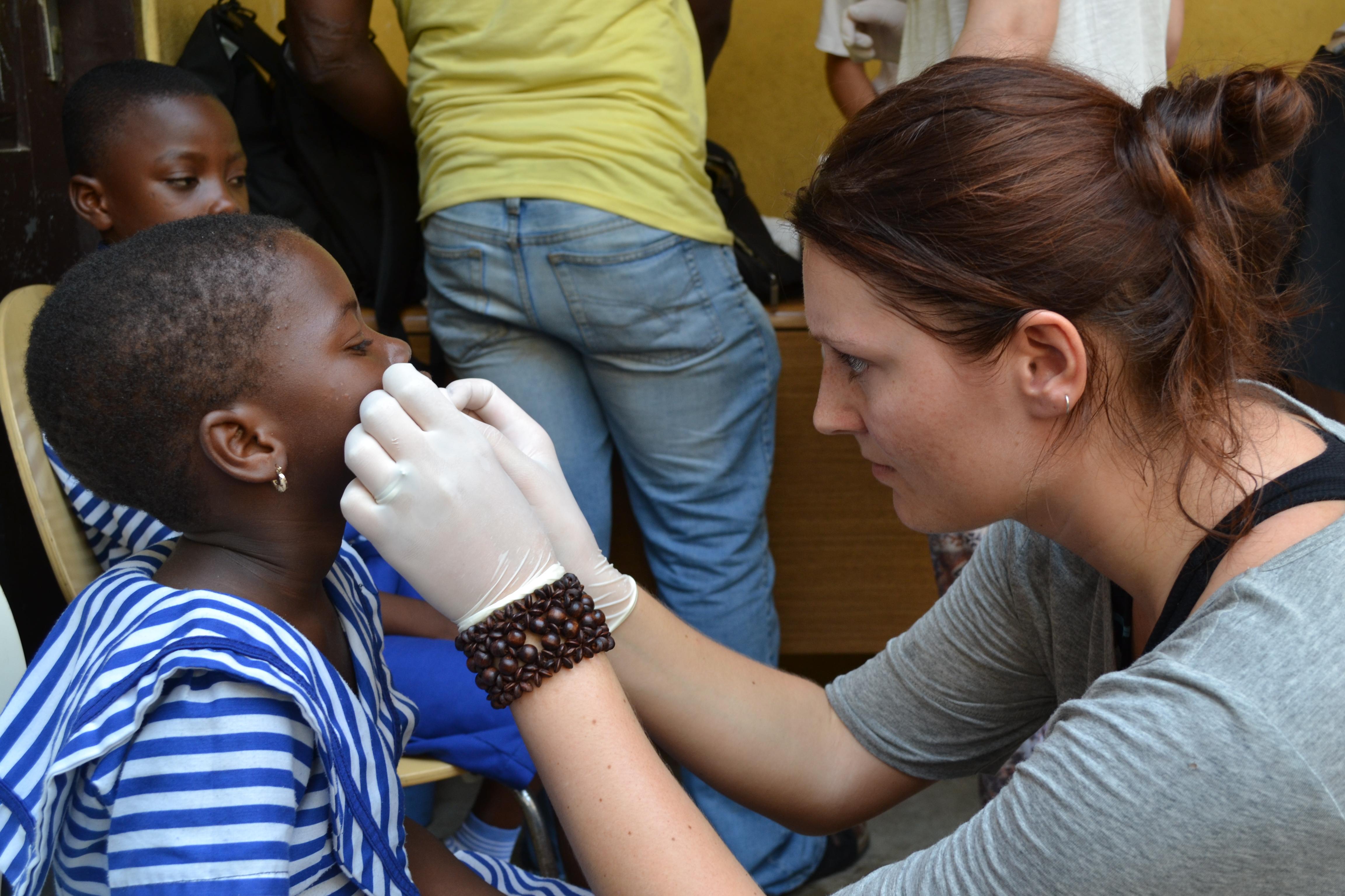 Projects Abroad healthcare intern is wearing white gloves to treat a child at a medical outreach in Ghana Child in Ghana is being treated on the face by a female healthcare intern at a medical outreach
